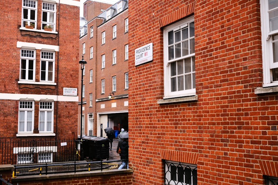 The image depicts the exterior of a building with a white stone facade, featuring an arched doorway with intricate detailing around the frame on the left side, and modern glass doors with metal handle