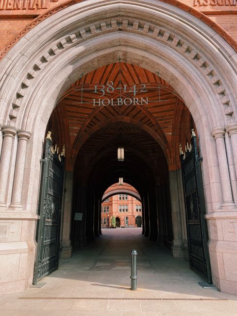 A close-up view of a building's exterior showing a white street sign that reads 'HIGH HOLBORN WC1' mounted on a cream-colored stone wall. To the left, there is a large, ornate wooden door with a semi-